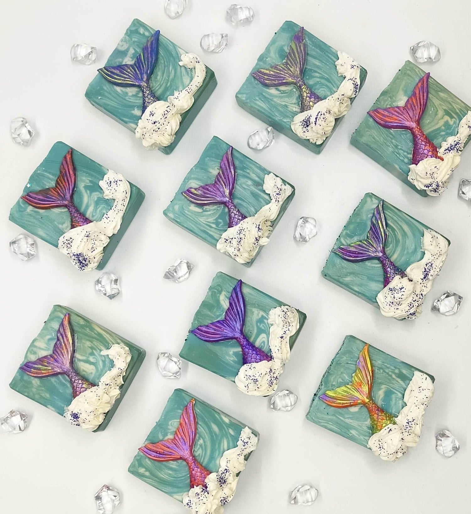 Flat lay of 10 brightly coloured mermaid-themed artisan soap bars arranged neatly.