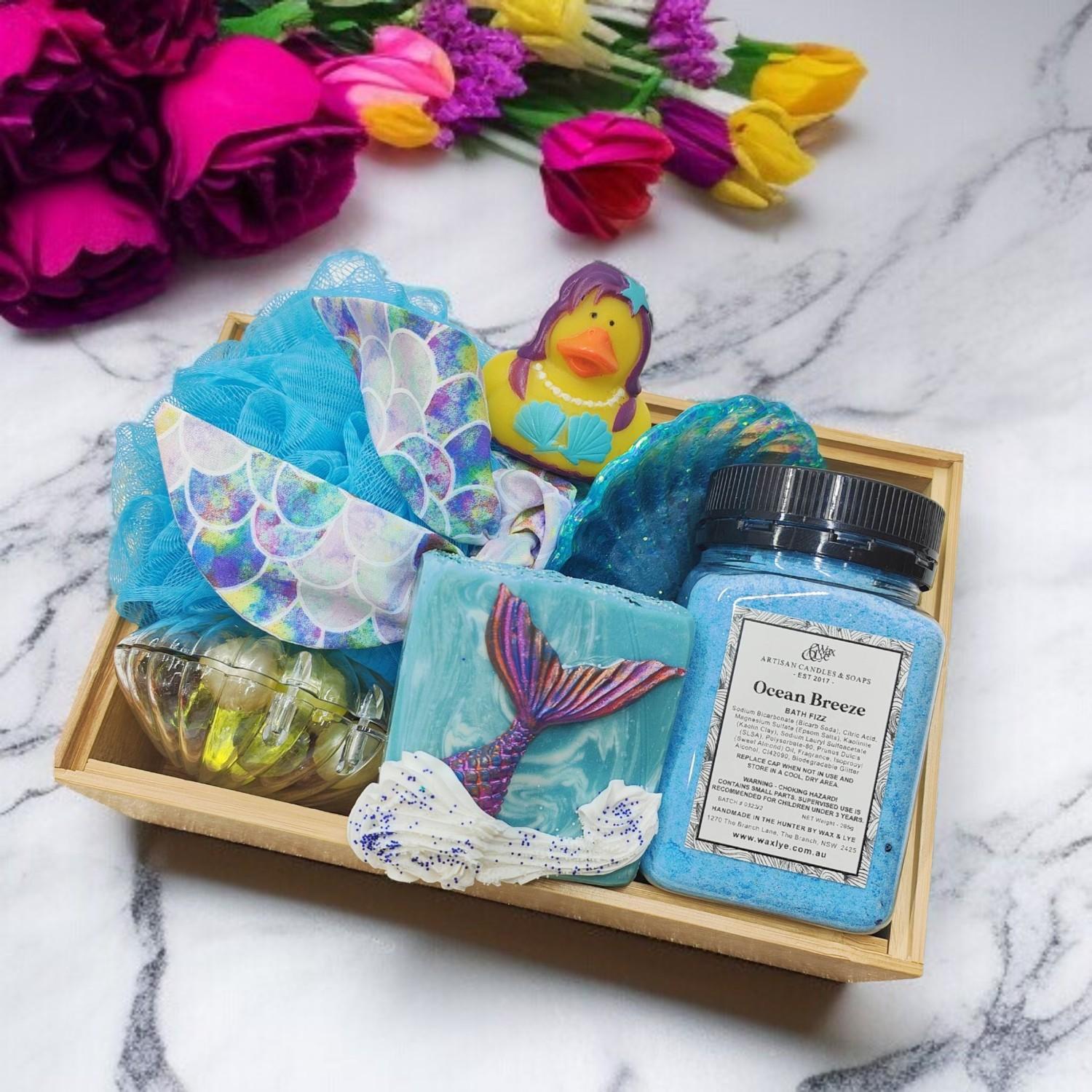 Mermaid-themed gift box filled with soap, bath fizz, and bath pearls, set against light marble and bright flowers