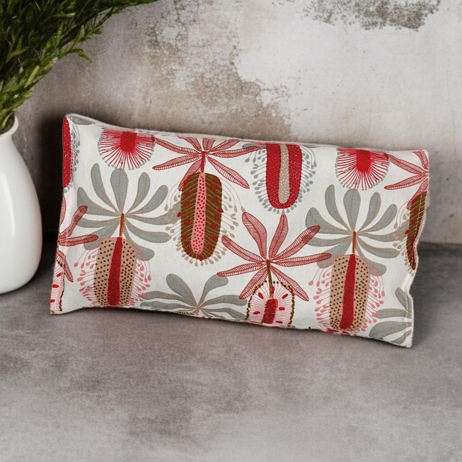 Handmade lupin heat bag with red and white banksia design resting against dark marble