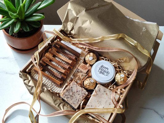 Gift basket with assorted items including a candle, chocolates, and soap on a marble surface.